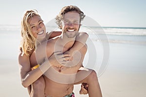 Portrait of young man piggybacking beautiful woman at beach