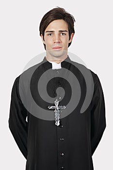 Portrait of young man in priest costume against gray background