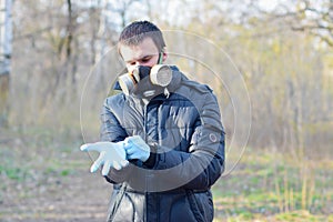 Portrait of young man in protective gas mask wears rubber disposable gloves outdoors in spring wood