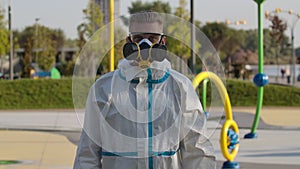 Portrait young man in a protective suit, glasses, a respirator and gloves holds a smartphone with green screen and