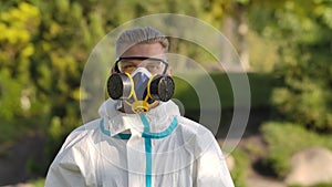 Portrait young man in a protective suit, glasses, a respirator and gloves holds a smartphone with green screen and