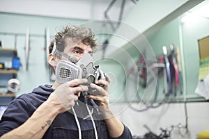 Portrait of a young man putting on a protective respirator mask in his workshop