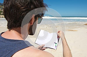 Portrait of a young man reading book at the beach