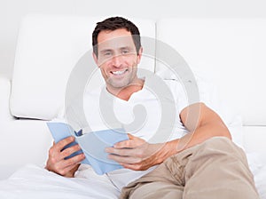 Portrait Of Young Man Reading Book On Bed