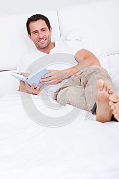 Portrait Of Young Man Reading Book On Bed