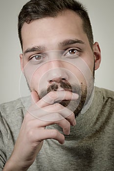 Portrait of a young man with a short beard in a moment of reflection with his hand to his chin