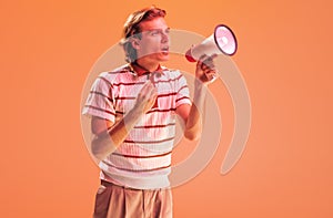 Portrait of young man shouting in megaphone isolated over orange studio background in neon light. Active speaker