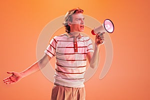 Portrait of young man shouting in megaphone isolated over orange studio background in neon light. Emotive, active speech