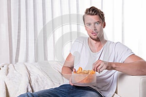 Portrait young man sitting on couch and eating chips