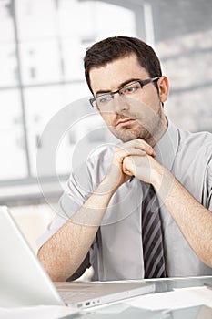 Portrait of young man sitting at desk using laptop