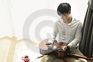 Portrait of young man sitting on floor with tablet for search lyrics in home.