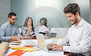 Portrait of young man sitting at his desk and working on laptop in the office.