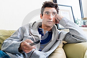 Portrait of young man sitting on the sofa while watching TV at h