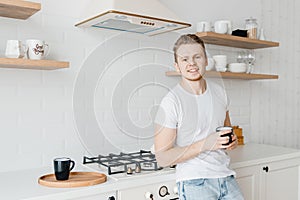 Portrait young man smiles drink fresh coffee in ceramic black mug breakfast. Bright kitchen background