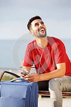 Young man smiling with suitcase and mobile phone