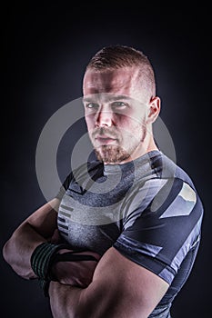 Portrait of a young man in sport outfit in fitness studio against dark background