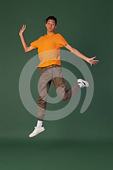 Portrait of young man, student in casual clothes jumping isolated on green vintage studio backgroud. Human emotions