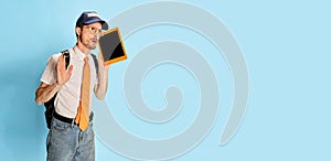 Portrait of young man, student in casual clothes posing with tablet  over blue background. Flyer