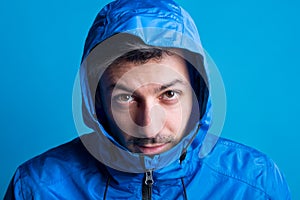 Portrait of a young man in a studio with anorak on a blue background.