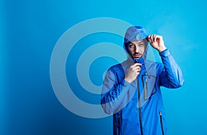 Portrait of a young man in a studio with anorak on a blue background.