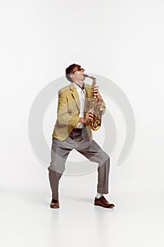 Portrait of young man in stylish yellow jacket playing saxophone isolated over white background. Jazz performer