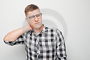 Portrait of young man suffering from pain, touching neck isolated on white studio background. Psychosomatics of stress