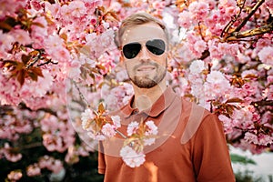 Portrait of young man in sunglasses with blooming sakura trees