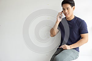 Portrait of young man talking on mobile phone. Handsome asian people smile while sitting speaking smartphone. Copy space grey back
