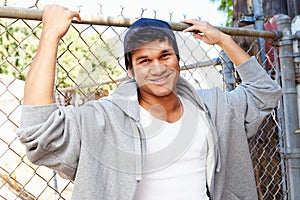 Portrait Of Young Man In Urban Setting Standing By Fence