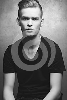 Portrait of a young man with very handsome face in black casual t-shirt and stylish haircut posing over silver metal  background.