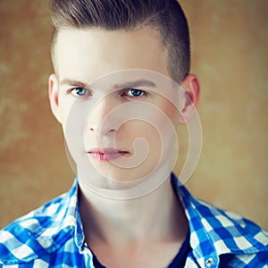 Portrait of a young man with very handsome face in blue casual shirt with stylish haircut posing over golden brown background.