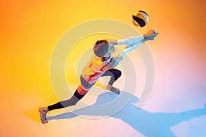 Portrait of young man, volleyball player in motion, kicking ball, playing  over yellow studio background in neon
