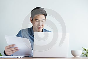 Portrait of young man wearing blue shirt is working with laptop and sitting at his desk  the office