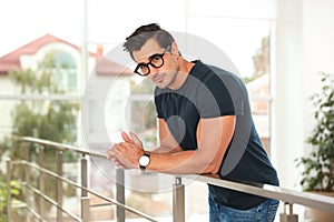 Portrait of  young man wearing glasses and leaning on railing indoors