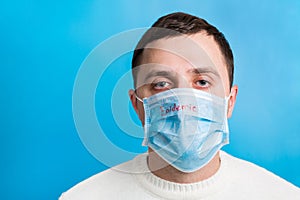 Portrait of young man wearing medical mask with epidemic word at blue background. concept. Respiratory protection