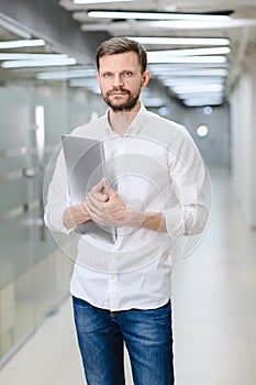 portrait of a young man in a white shirt in the office. The manager in the office is holding a laptop