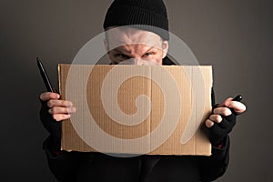 Portrait a young man who holds a felttip pen in his mouth to write text on cardboard. begging concept