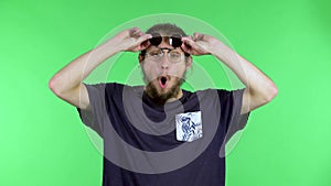 A portrait of a young man who lifts the dark lenses of his sunglasses with an enthusiastic and surprised expression