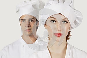 Portrait of young man and woman in chef`s uniform against gray background