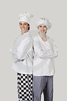 Portrait of young man and woman in chef`s uniform with arms crossed against gray background