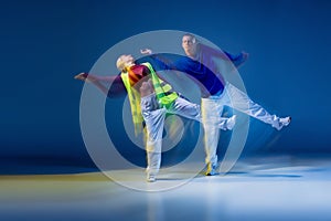 Portrait of young man and woman dancing isolated over dark blue background with mixed lights. Synchronic