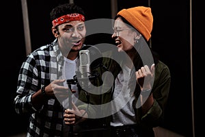 Portrait of young man and woman, duet singing into a condenser microphone while recording a song in a professional