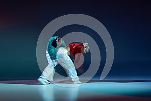 Portrait of young man and woman, hip-hop dancers performing on stage isolated over dark blue background with mixed