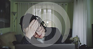 Portrait of young man working in front of computer at home, talking to a group chat via headset. Male freelancer being