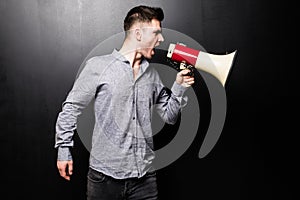 Portrait of young handsome man yelling into the megaphone over black background