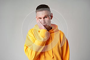 Portrait of young man in yellow hoodie with face palm gesture on gray background