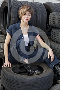Portrait of a young mechanic sitting on tires in car workshop