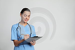 Portrait of young medical assistant with stethoscope and clipboard on color background