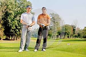 Portrait of young men standing with golf sticks on golf course