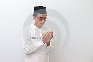 Portrait of young millennial Asian muslim man praying earnestly with his hands raised. Isolated image on white background